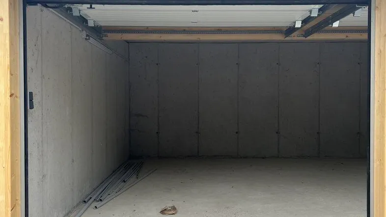 Leere Garage mit Betonwänden, Holzelementen am Eingang und Betonboden in neuwertigem Zustand.
