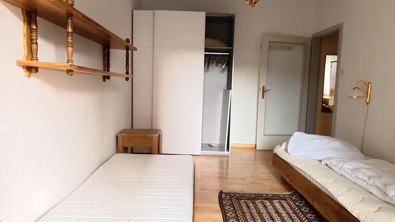 Helles Schlafzimmer mit Parkettboden, zwei Matratzen und einem weißen Kleiderschrank.