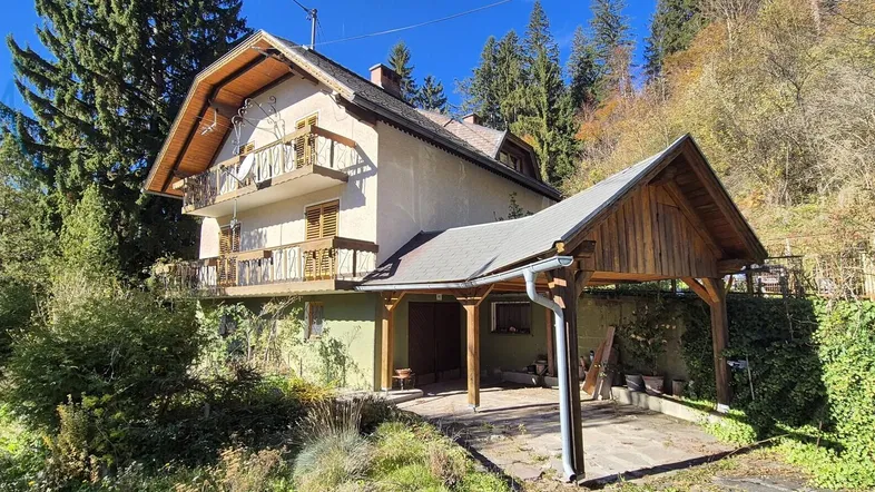 Traditionelles Haus mit Holzbalkonen und einem überdachten Carport in grüner Umgebung.