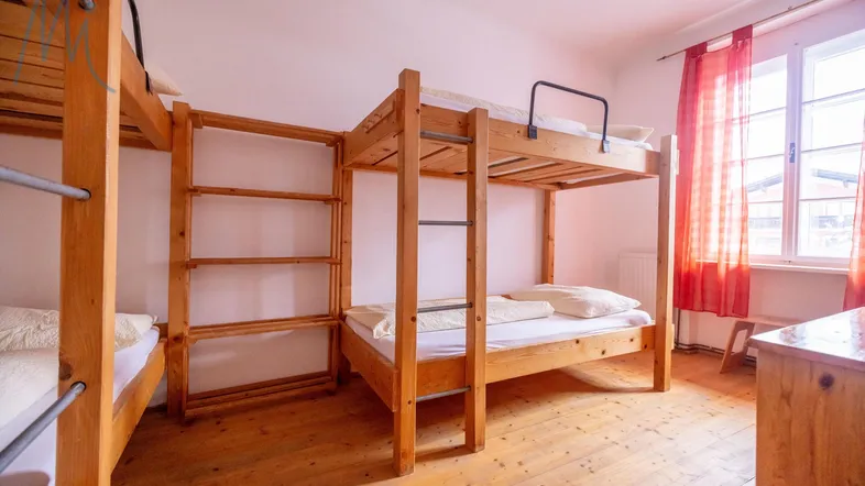 Einfaches Schlafzimmer mit mehreren Holz-Etagenbetten und einem Fenster mit roten Vorhängen, ideal für Gruppenunterkünfte.