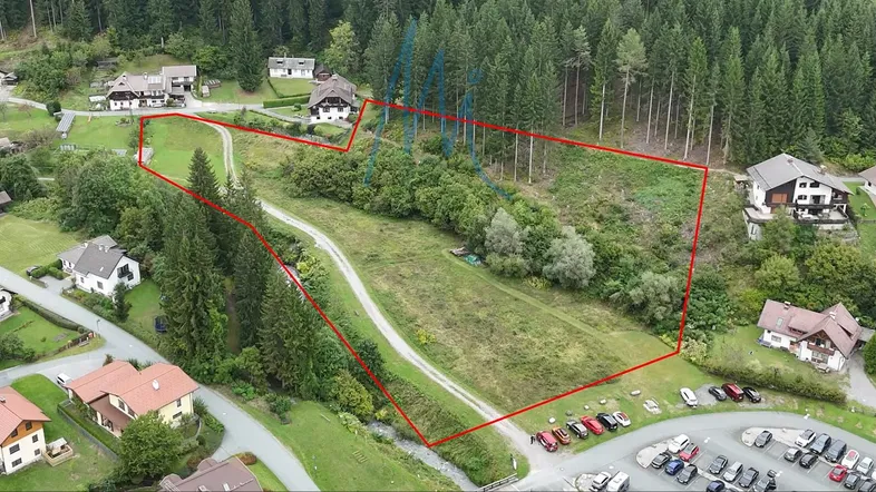 Luftaufnahme eines großen Grundstücks, umgeben von Wald und einigen Häusern, mit einem Feldweg und Parkplätzen.