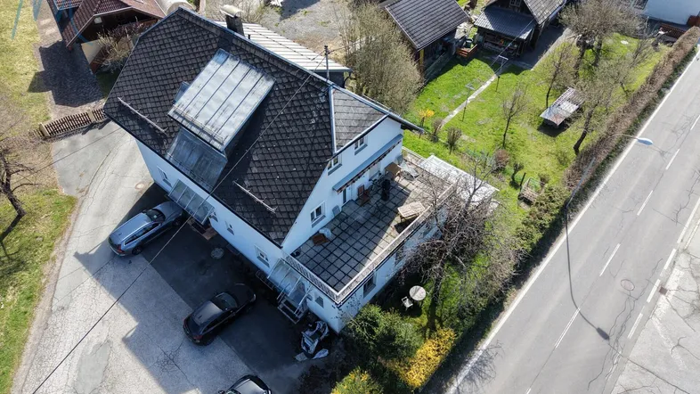 Luftaufnahme eines Wohnhauses mit Satteldach, angrenzender Terrasse und Parkplätzen an der Straße.