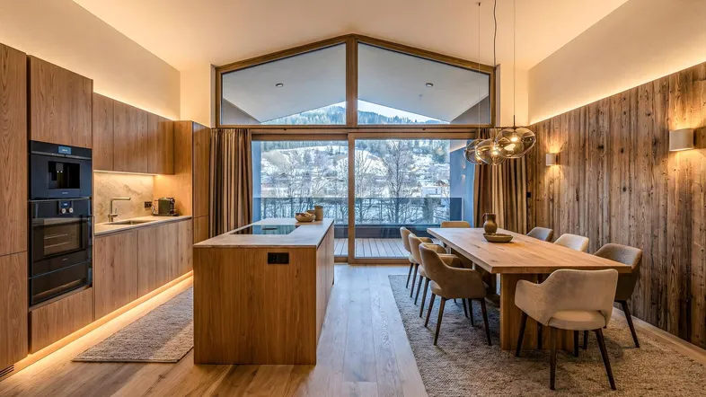 Moderne offene Küche und Essbereich mit Holzelementen und Bergblick durch große Fenster.