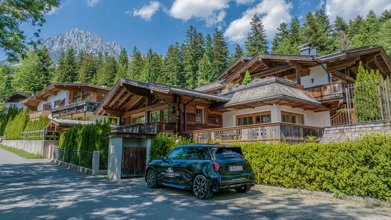 Mehrere luxuriöse Chalets im alpinen Stil mit Holzbalkonen und Bergblick unter blauem Himmel.