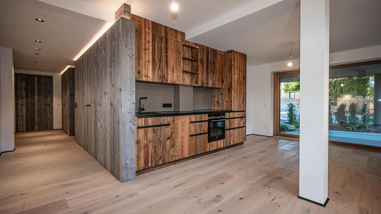 Moderne Küche mit Holzfronten, dunkler Arbeitsplatte und hellem Holzboden in einem offenen Wohnbereich.