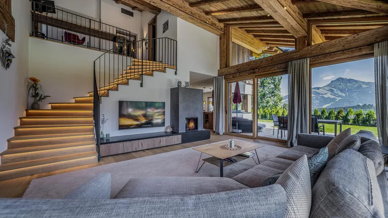 Großzügiges Wohnzimmer mit hohen Decken, Holzbalken, Kamin und beeindruckendem Bergblick.