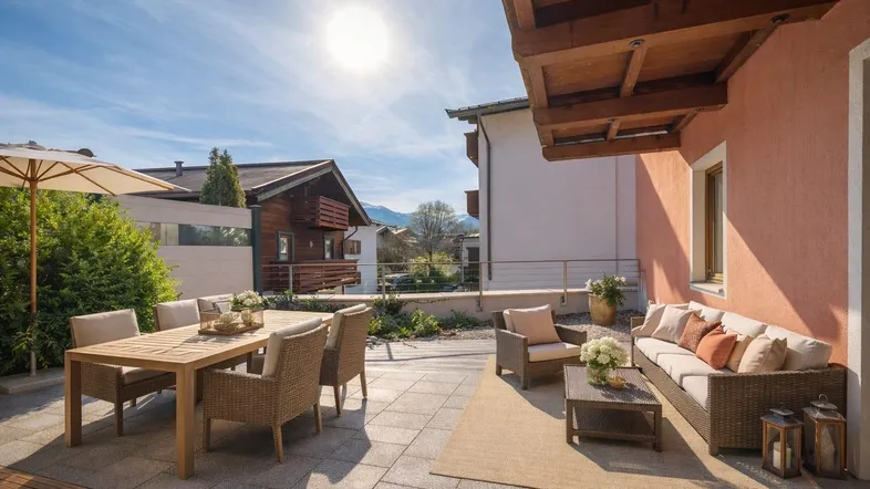 Sonnige Terrasse mit bequemen Gartenmöbeln und Essbereich, umgeben von alpiner Architektur.