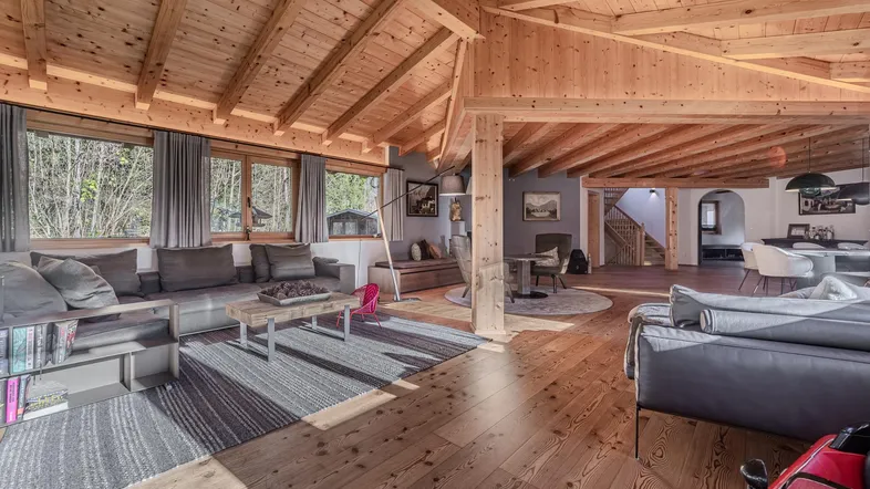 Geräumiger offener Wohnbereich mit Holzbalkendecke, großen Fenstern und gemütlicher Einrichtung.