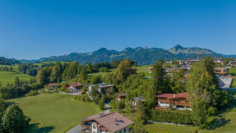 Luftaufnahme eines malerischen Dorfes in den Bergen mit grünen Wiesen und traditionellen Häusern.