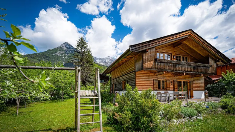 Traditionelles Holzhaus in den Bergen mit Garten und Bergblick unter blauem Himmel.