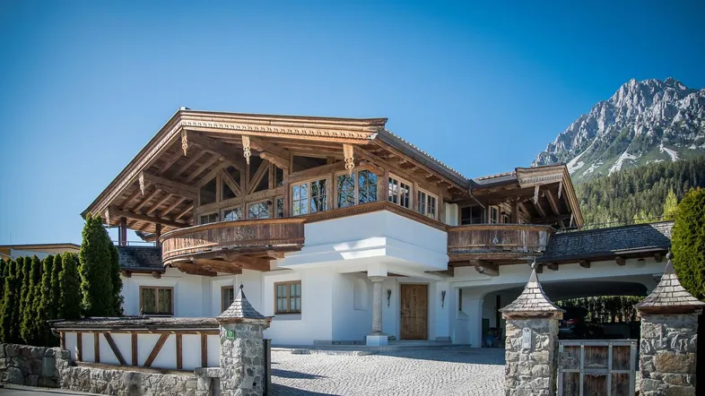 Beeindruckendes Chalet im alpinen Stil mit Holzbalkonen und majestätischem Bergblick unter blauem Himmel.