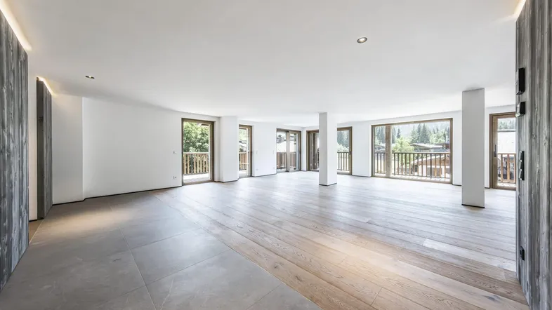 Helles, offenes Wohnzimmer mit Holzboden und Zugang zu mehreren Balkonen mit Bergblick.