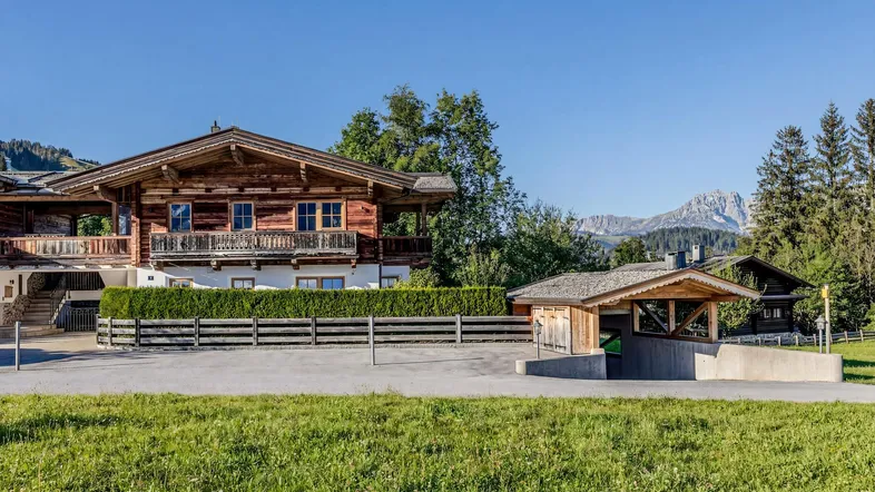 Traditionelles Holzhaus im alpinen Stil mit Balkonen, umgeben von grüner Landschaft und Bergblick.