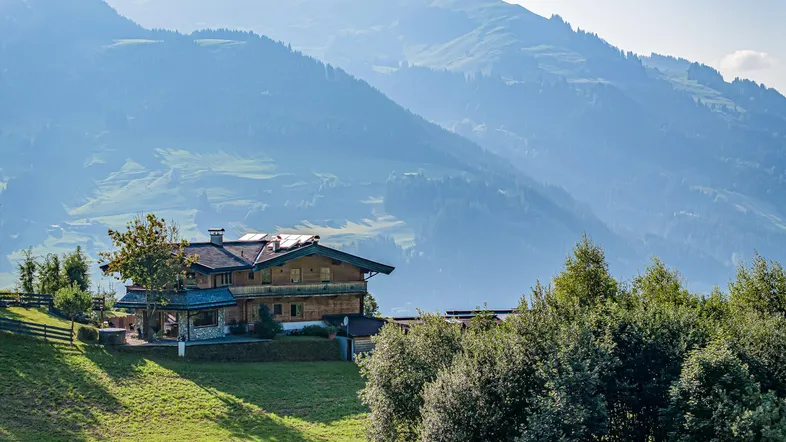 Charmantes Chalet in alpiner Landschaft mit grünen Hügeln und Bergblick unter blauem Himmel.