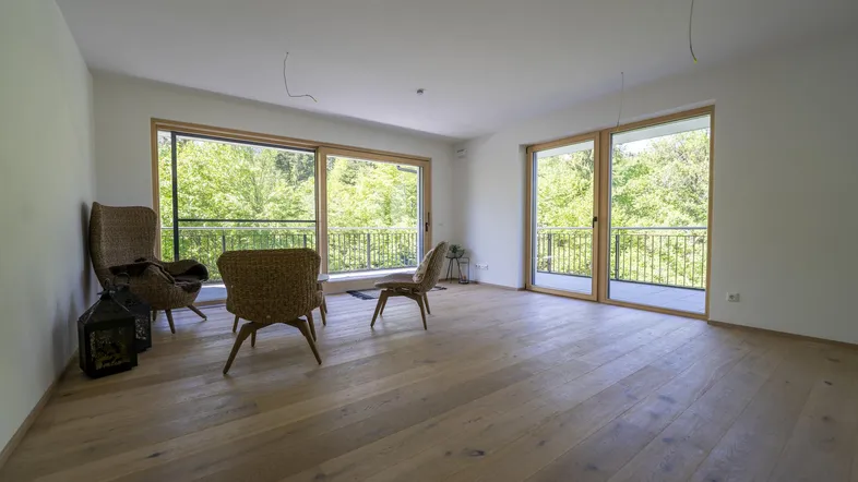 Helles Wohnzimmer mit Eichenparkettboden und großen Schiebetüren, die zu einem Balkon mit grüner Aussicht führen.
