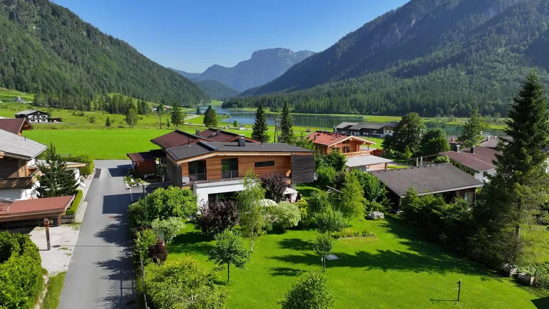 Luftaufnahme eines modernen Hauses in einer malerischen Berglandschaft mit See im Hintergrund.