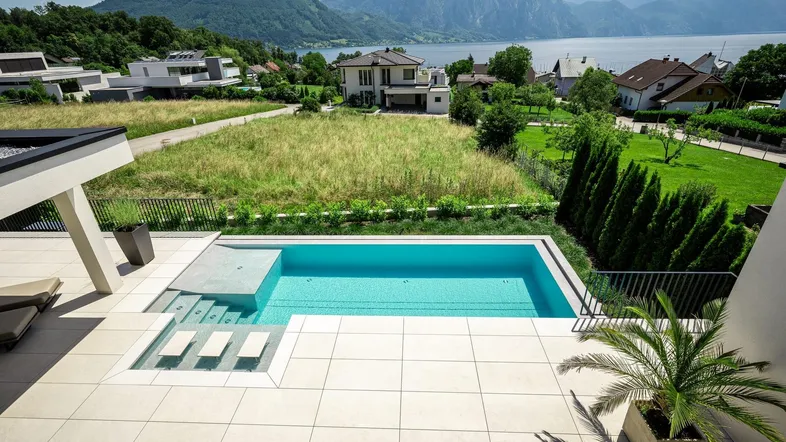 Moderner Außenbereich mit Infinity-Pool, großzügiger Terrasse und atemberaubendem Blick auf den See und die Berge.