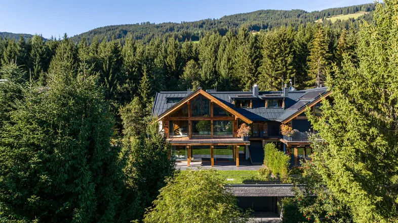 Luxuriöses Chalet mit moderner Architektur, großen Glasfronten und Bergblick, umgeben von dichtem Wald.