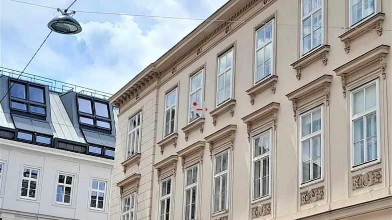 Historische Fassade eines Altbaus mit verzierten Fenstern und einem modernen Dachausbau im Hintergrund.