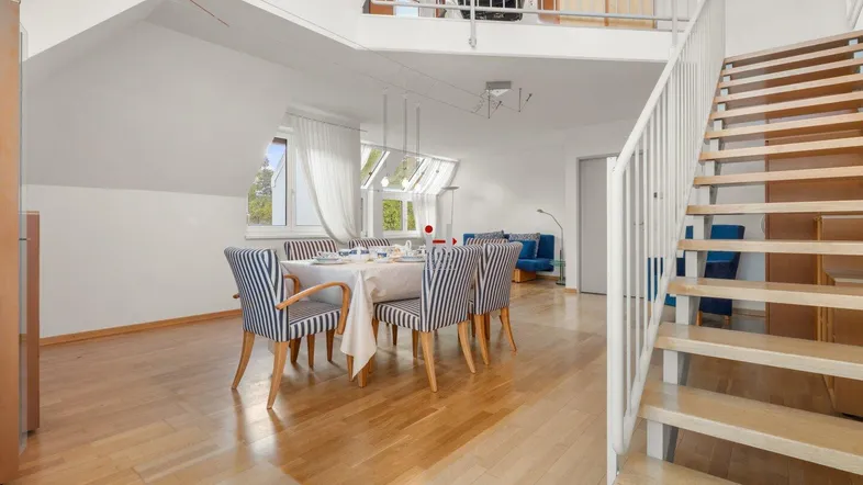 Heller Wohn- und Essbereich mit Holzboden, Dachschrägen und einer offenen Treppe zur Galerie.