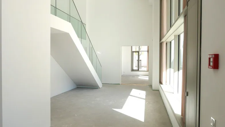 Heller, unmöblierter Eingangsbereich mit moderner Treppe und großen Fenstern, noch im Bau.
