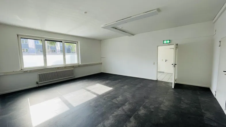 Geräumiges Büro mit dunklem Vinylboden, großen Fenstern und viel Tageslicht.