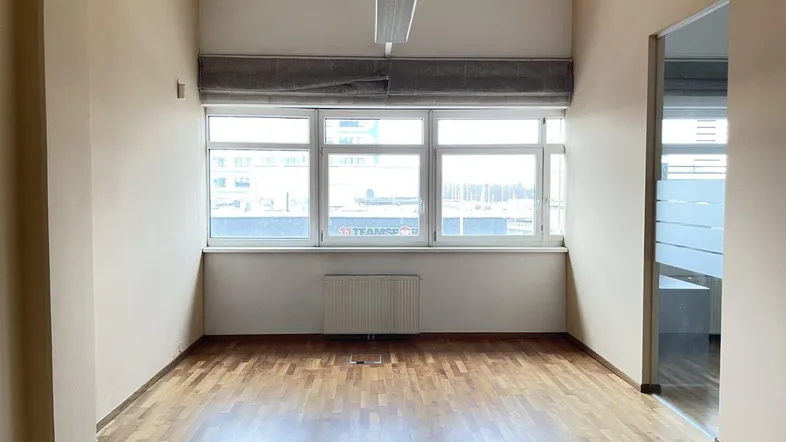 Heller Büroraum mit großen Fenstern, Holzparkettboden und Heizkörper unter der Fensterbank.