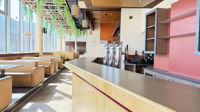 Geräumiger Restaurantbereich mit langer Theke, Zapfanlage und großen Fenstern, die viel Tageslicht hereinlassen.