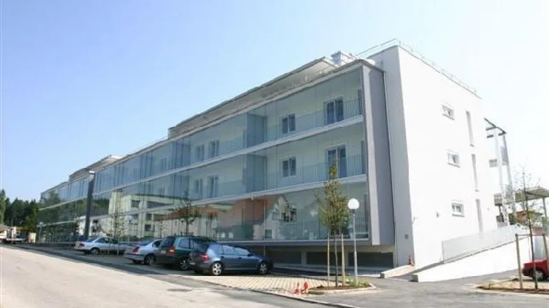 Moderne Wohnanlage mit Glasbalkonen und Parkplätzen vor dem Gebäude.