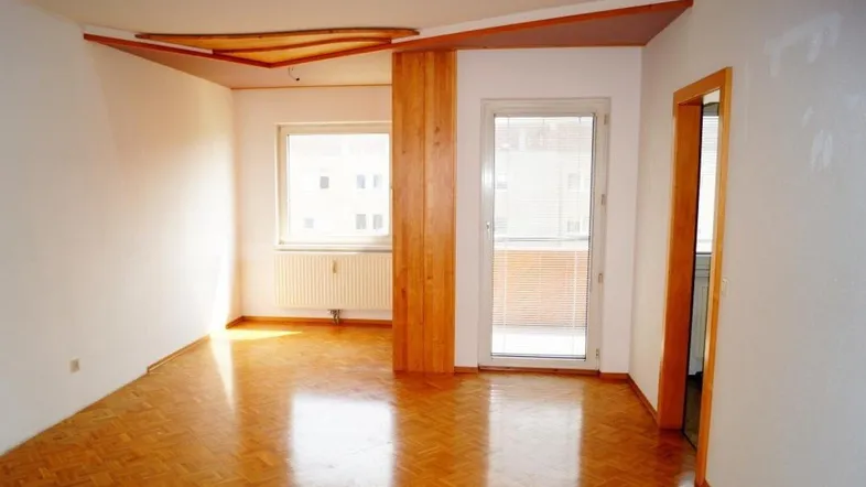 Heller, unmöblierter Wohnraum mit Parkettboden, dekorativer Decke und Zugang zum Balkon.