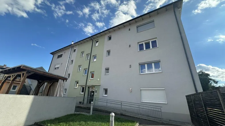 Modernes Mehrfamilienhaus mit heller Fassade, Rampe am Eingang und gepflegter Außenanlage.