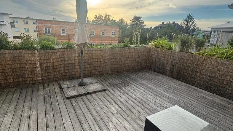 Große Holzterrasse mit Sonnenschirm und Sitzgelegenheiten, ideal für entspannte Stunden im Freien.