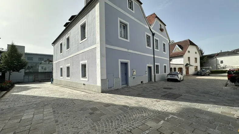 Historisches Gebäude mit hellblauer Fassade und gepflastertem Vorplatz unter klarem Himmel.