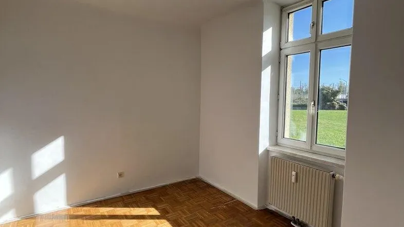 Helles Zimmer mit Parkettboden und Blick ins Grüne, ideal als Wohn- oder Schlafzimmer.