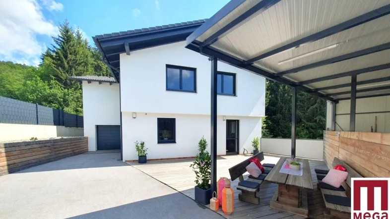 Moderne Hausfassade mit überdachtem Essbereich im Freien und Blick ins Grüne.