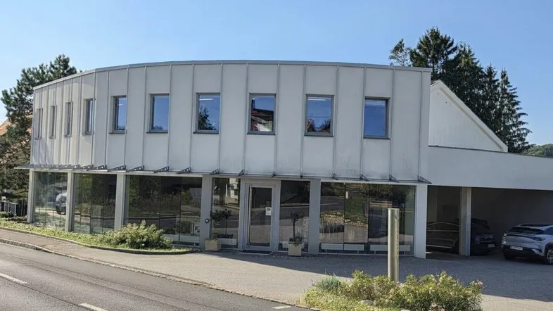Modernes Geschäftsgebäude mit runder Fassade und großen Schaufenstern an einer Straße gelegen.