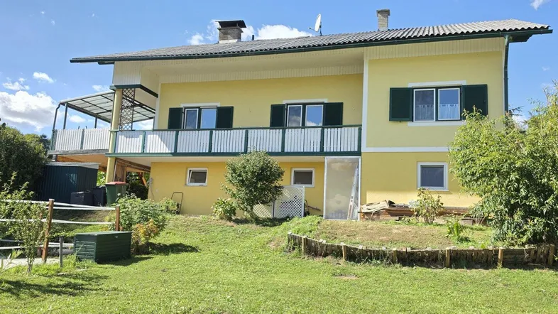 Gelbes Einfamilienhaus mit Balkon, grünen Fensterläden und großem Gartenbereich.