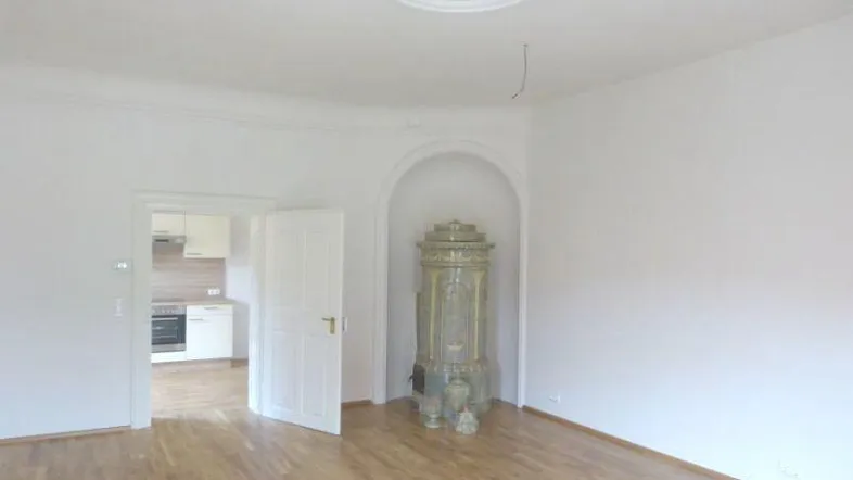 Helles Wohnzimmer mit Parkettboden, Stuckdecke und einem traditionellen Kachelofen in einer Nische.