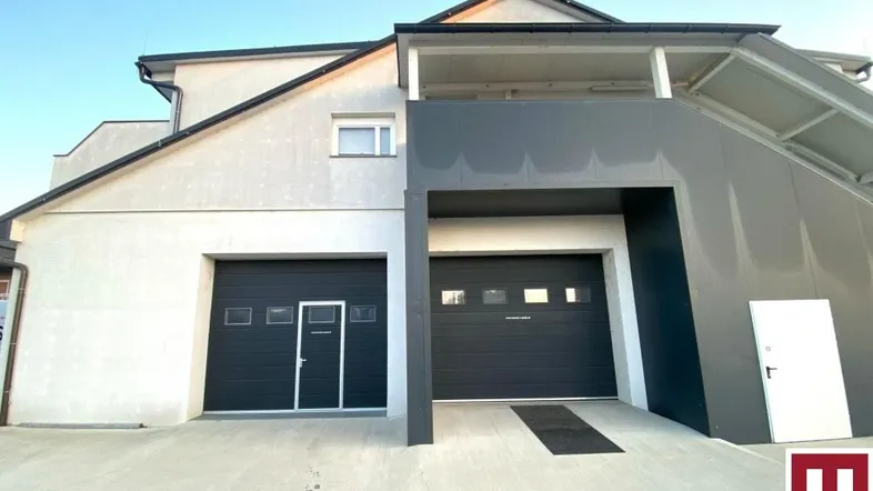 Moderne Gebäudefassade mit zwei Garagentoren und einer Zufahrt, die zu den Parkplätzen führt.