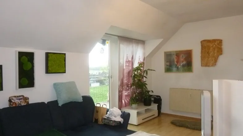 Gemütliches Wohnzimmer mit Dachschrägen, Holzboden und Zugang zu einem Balkon mit Weitblick.