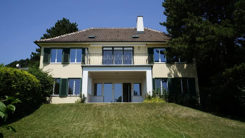 Elegantes Haus mit gelber Fassade, grünen Fensterläden und kleinem Balkon.