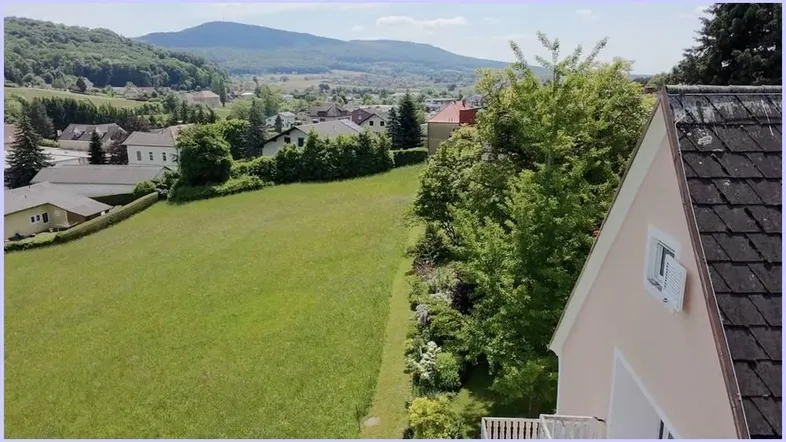 Weitläufiger Blick über grüne Landschaft und umliegende Häuser mit Bergen im Hintergrund.