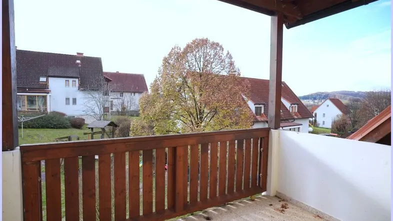 Geräumiger Balkon mit Holzbalken und Blick auf die umliegende Wohngegend und grüne Landschaft.