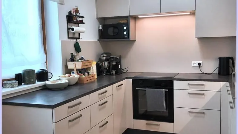Moderne Küche mit hellgrauen Schränken, dunkler Arbeitsplatte und Parkettboden.