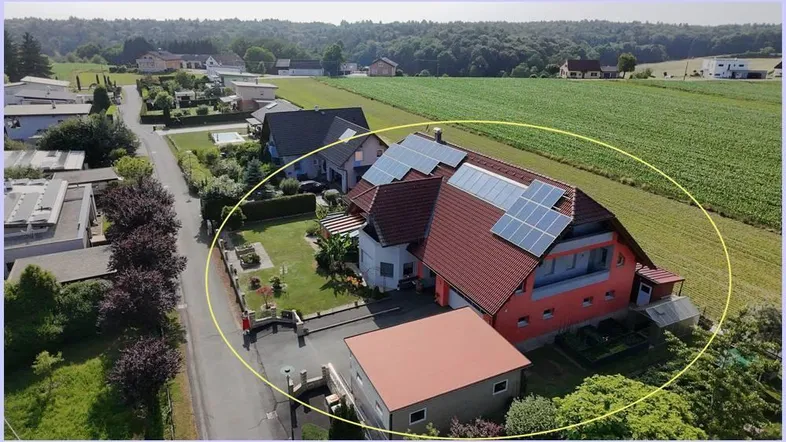 Luftaufnahme des Hauses mit Photovoltaikanlage auf dem Dach und umliegender grüner Landschaft.