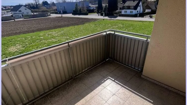 Geräumiger Balkon mit Fliesenboden und Markise, bietet einen weiten Blick ins Grüne.