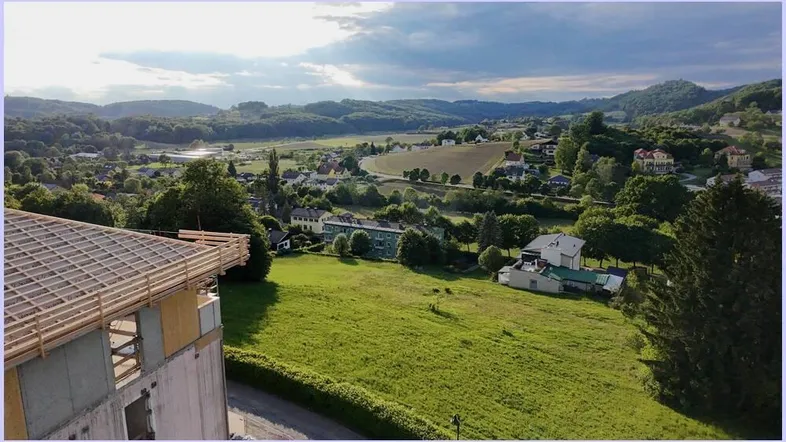 Blick auf ein im Bau befindliches Gebäude mit weitem Ausblick über eine grüne Hügellandschaft.