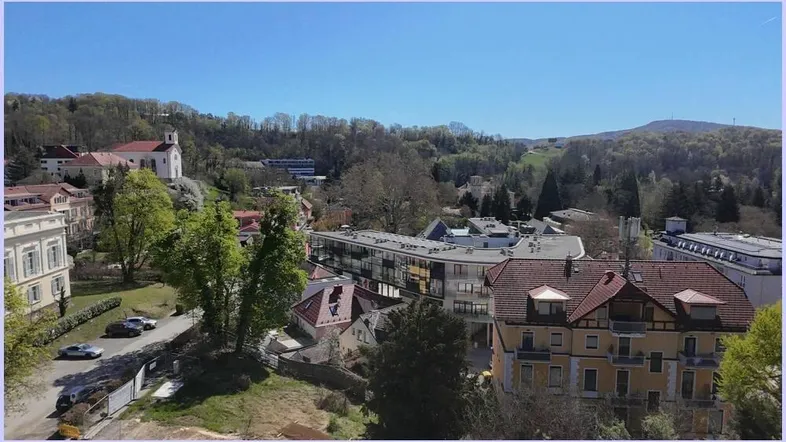 Panoramablick über eine malerische Stadt mit historischen Gebäuden und grünen Hügeln im Hintergrund.