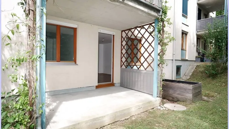 Überdachte Terrasse mit Gitterrankhilfe und Zugang zu einem kleinen Gartenbereich.