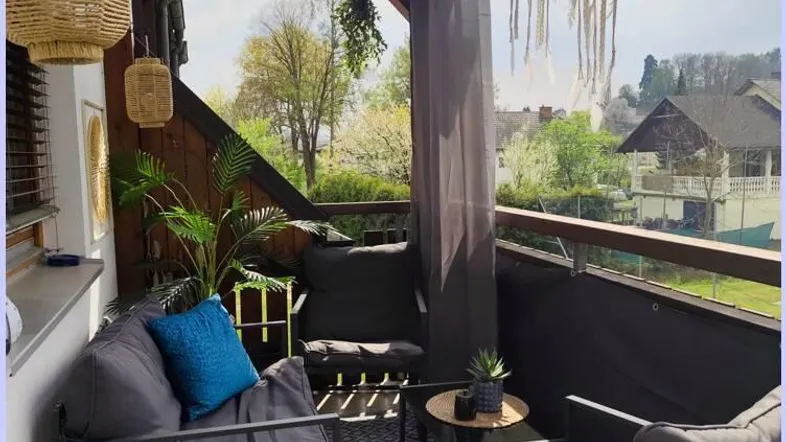 Gemütlicher Balkon mit bequemen Sitzmöbeln, Vorhängen und Blick ins Grüne.